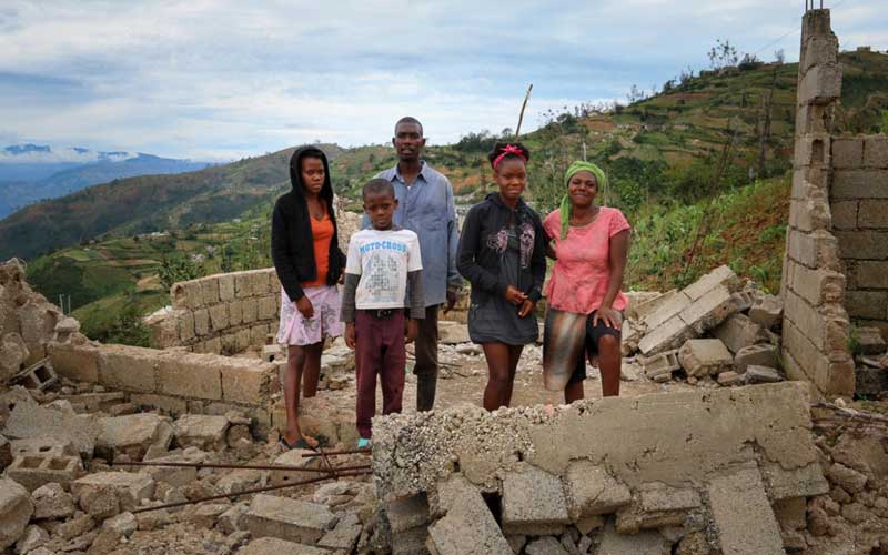 A family in Haiti stands in the rubble of their devastated home on a hillside.