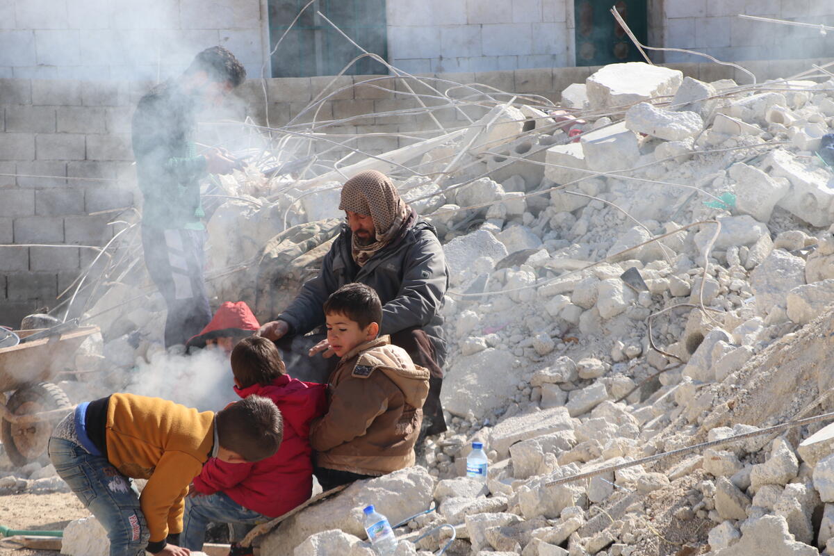In Syria, a man and four small children warm themselves around a fire made in a large pile of rubble.