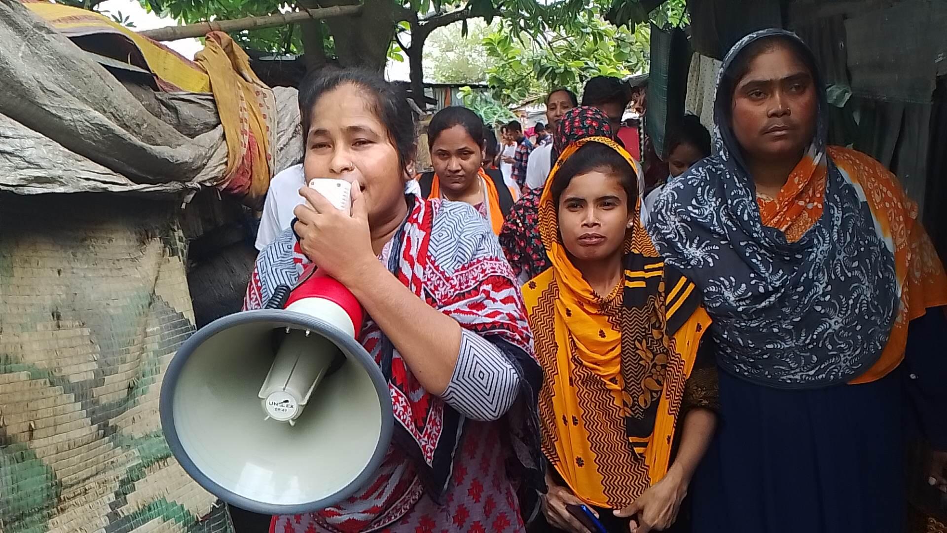 A woman shouts into a megaphone as she and others move through a group of makeshift shelters.