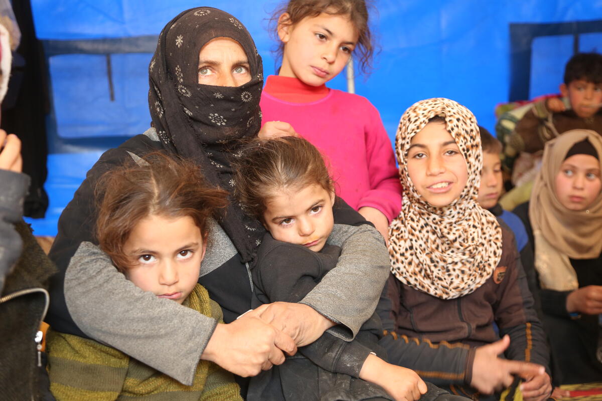 A Syrian mother hugs her two daughters, with two other daughters sitting beside her.