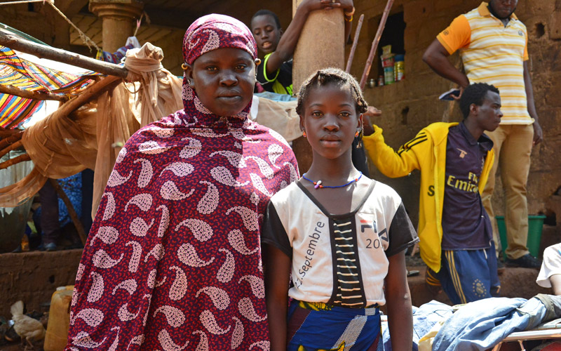 A mother and daughter from Mali look at the camera. They are in a busy marketplace.