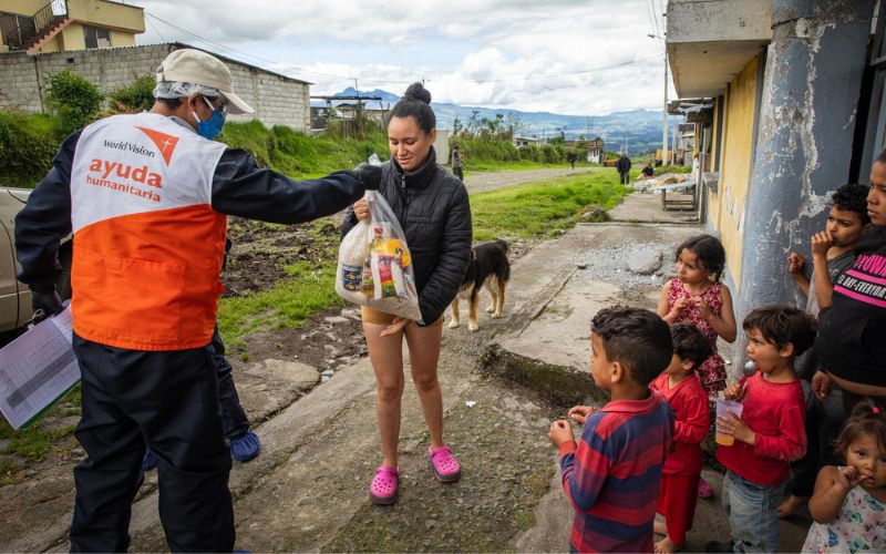 A World Vision team member hands a bag of food supplies to a woman in Ecuador. Seven children stand nearby.