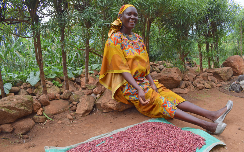 A Kenyan woman smiles as she sits next to iron-fortified beans that she grew and is now drying.