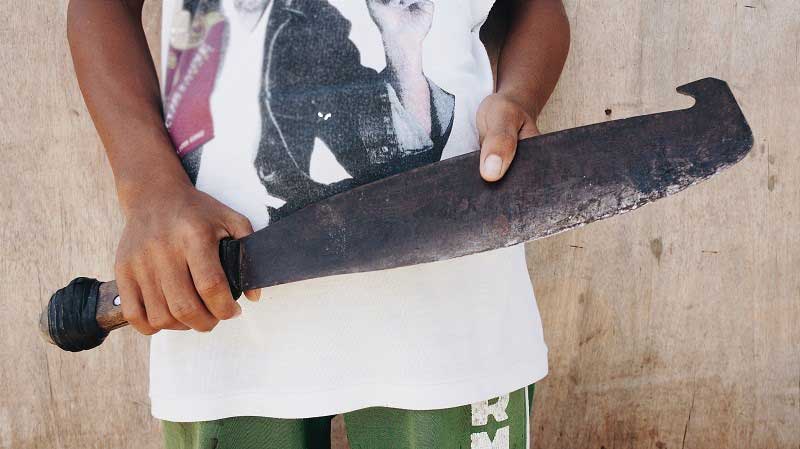 Close-up shot of a boy’s hands, holding the rusty machete he once used to harvest sugar cane.