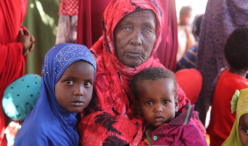 An elderly woman holds two young children in her lap in east Africa.