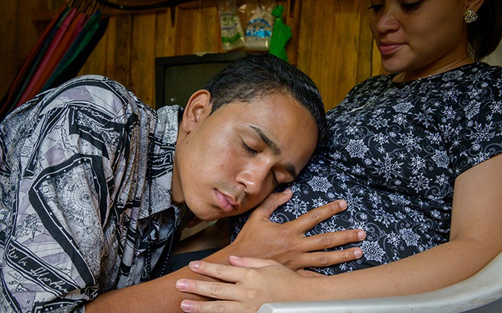 A young man rests his head on the belly of a pregnant woman. His eyes are closed; his face looks peaceful.