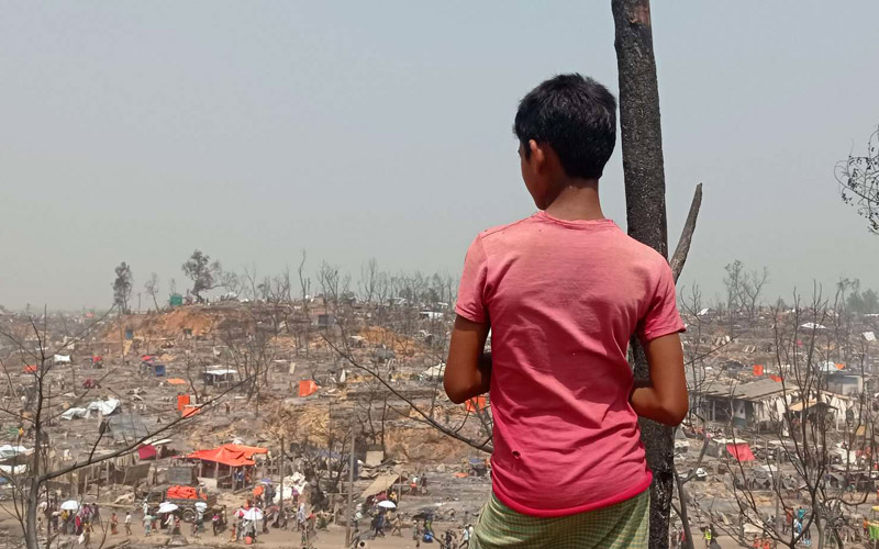 a young rohingya boy looks out over a burned landscape