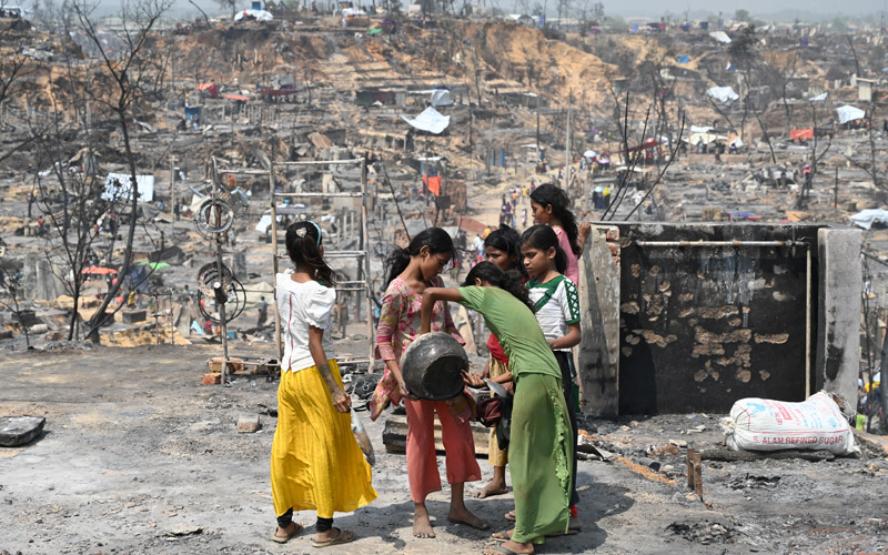 a group of adolescent girls sift through burned debris for what they can slavage.