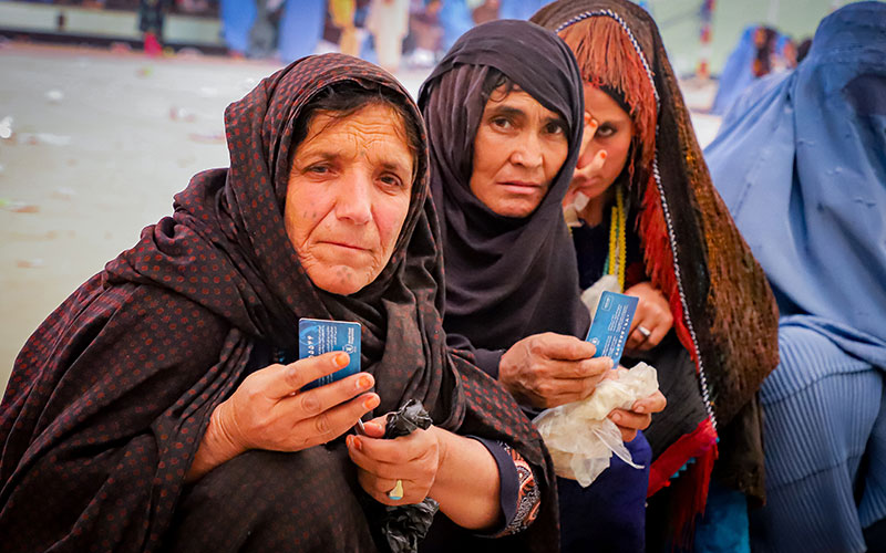 In Afghanistan, women wait with their identification cards for cash assistance to buy food.