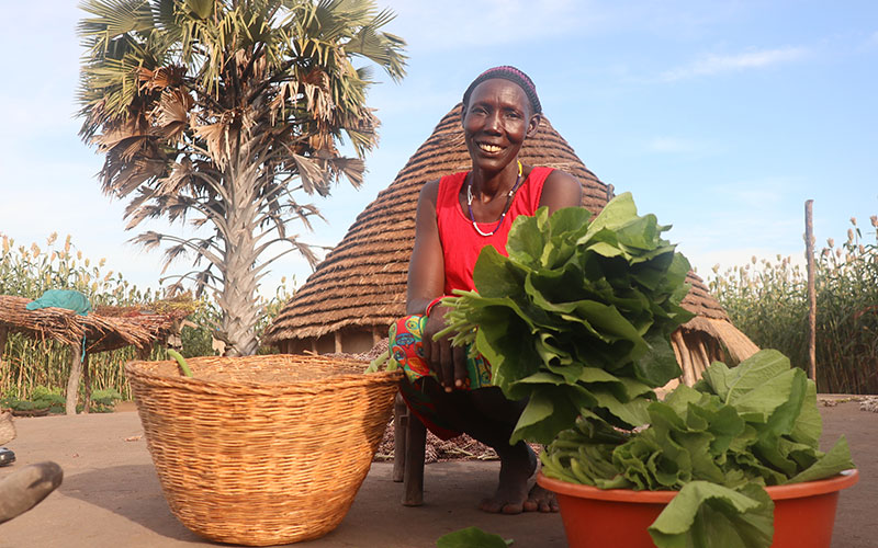 In South Sudan a woman in red shows off the huge green leafy vegetables she has grown.