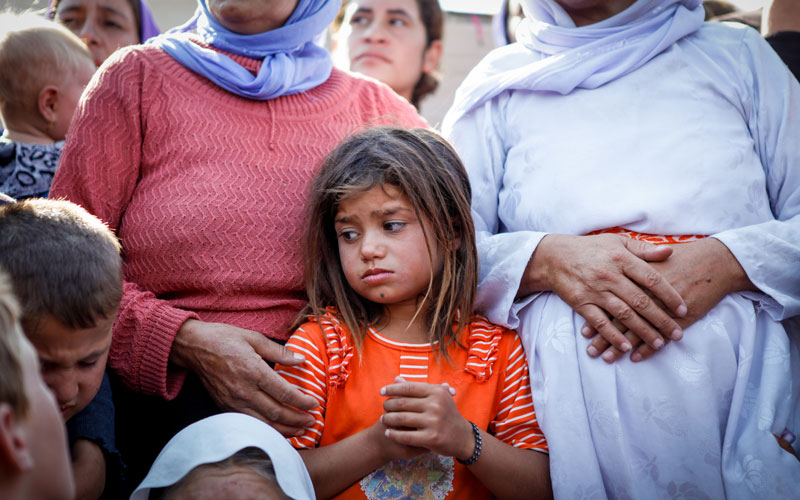 A girl folds her hands and looks worried. Beside her, a little boy cries.