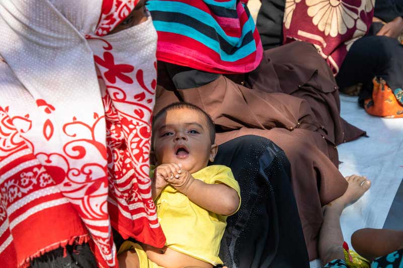 A mother in Bangladesh in a white and red niqab sits cradling her infant in her lap.