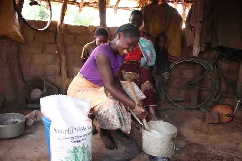 A woman in a purple shirt cooks for her family using crops she received from World Vision in her kitchen in Zambia.