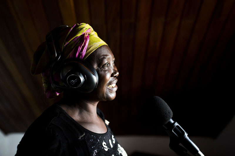 A woman wearing a yellow and pink head scarf used a pair of headphones and record music in a studio.