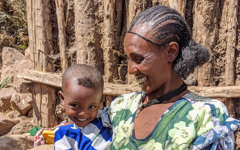An Ethiopian woman smiles at the baby she holds. The baby smiles at the camera.