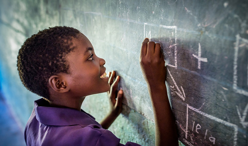 A girl in a navy uniform smiles as she writes out a math problem on the chalkboard.