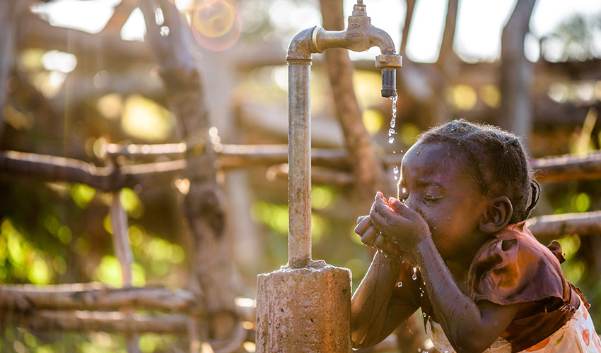 Little girl with braids uses her hands to drink water from an outdoor faucet.