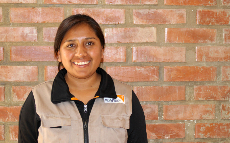 A young woman in a World Vision vest in front of a brick wall