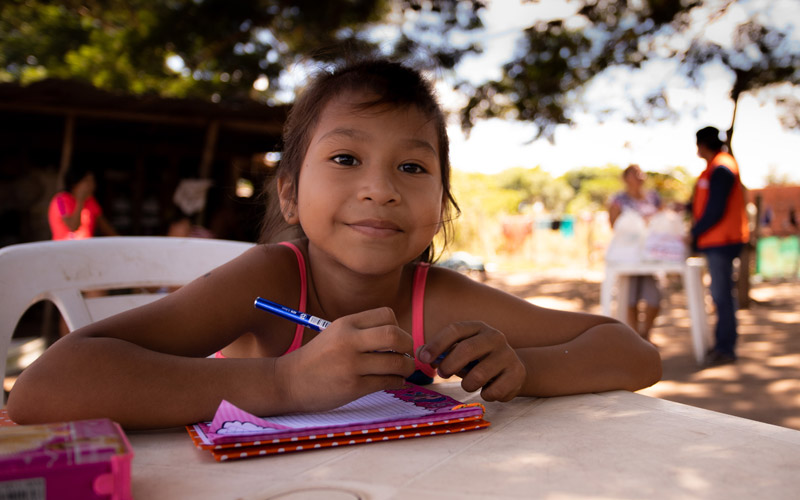 A young Bolivian girls sits at a desk with booklet and smiles
