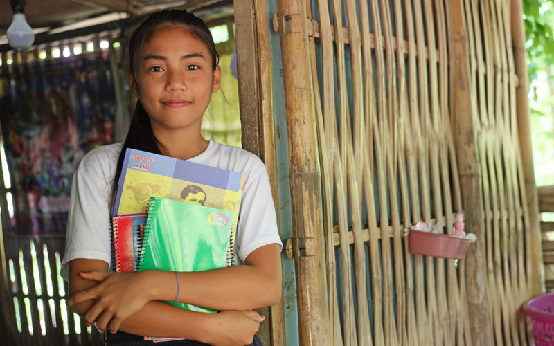 A young Philippina girl stands in a doorway carrying books