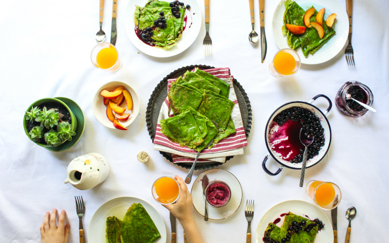 A table set with green pancakes, blueberries and orange juice.
