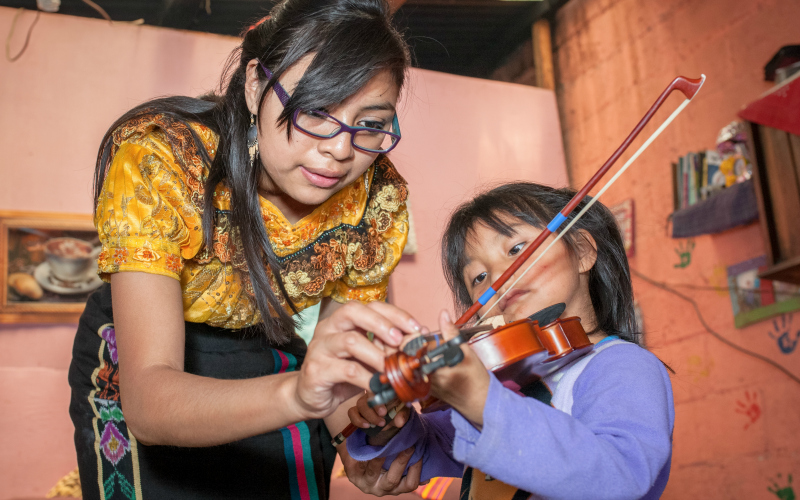 A young woman helps a little girl hold her violin