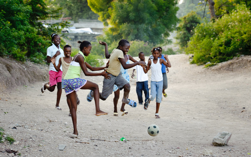 A group of Haitian children play soccer outside.