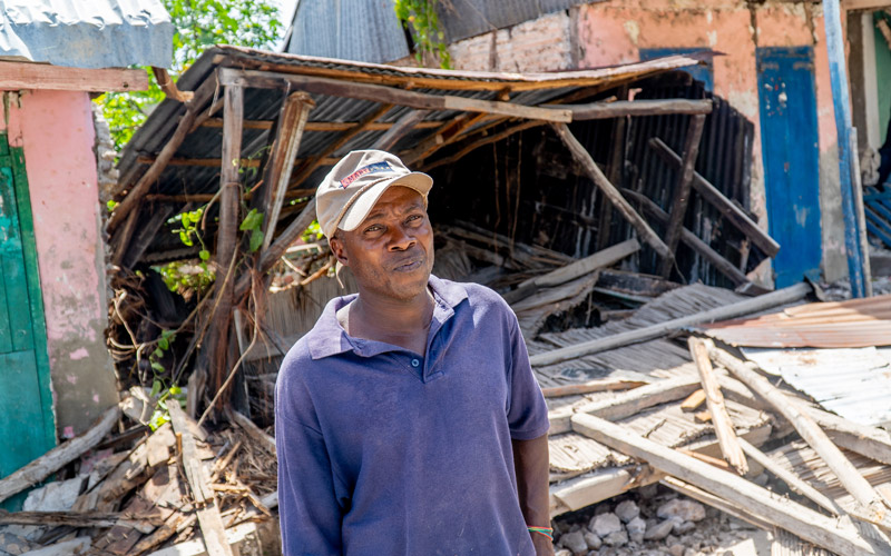 A Haitian man stands outside the ruins of what was his home.