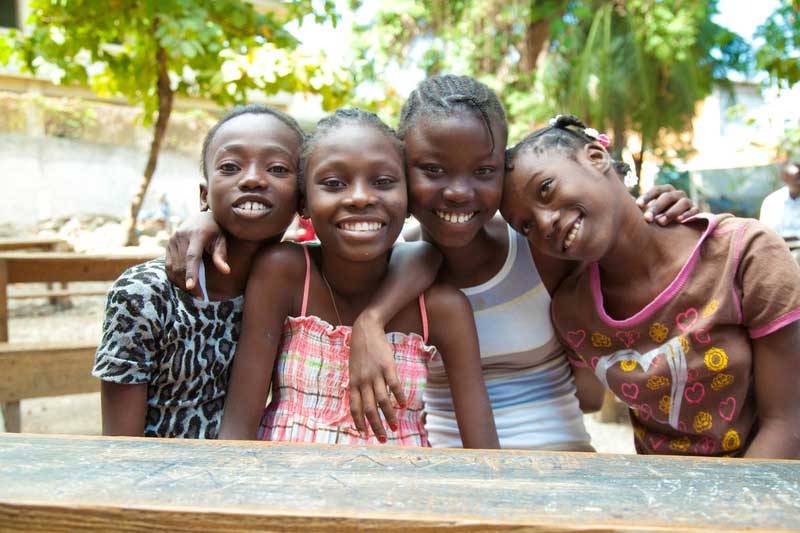 Four Haitian school-aged girls smile to the camera