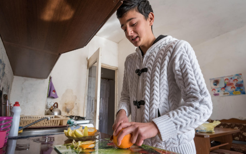A young man cuts fruit in his kitchen in Armenia.