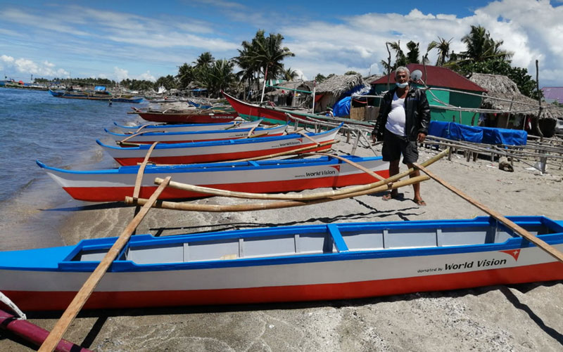 A row of small boats lines a beach in the Philippines. A man stands beside them.