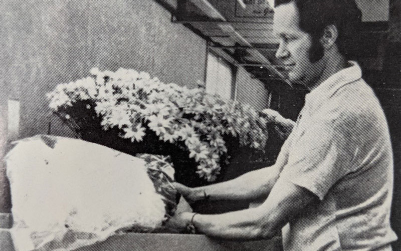 Black-and-white image of a man packaging flowers for delivery.