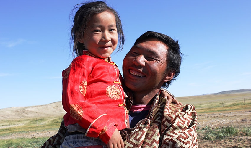 mongolian father holds his young daughter and looks at her smiling