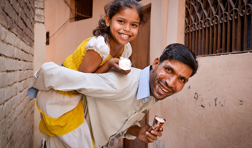 a dad in india gives his daughter a piggyback while they eat ice cream cones