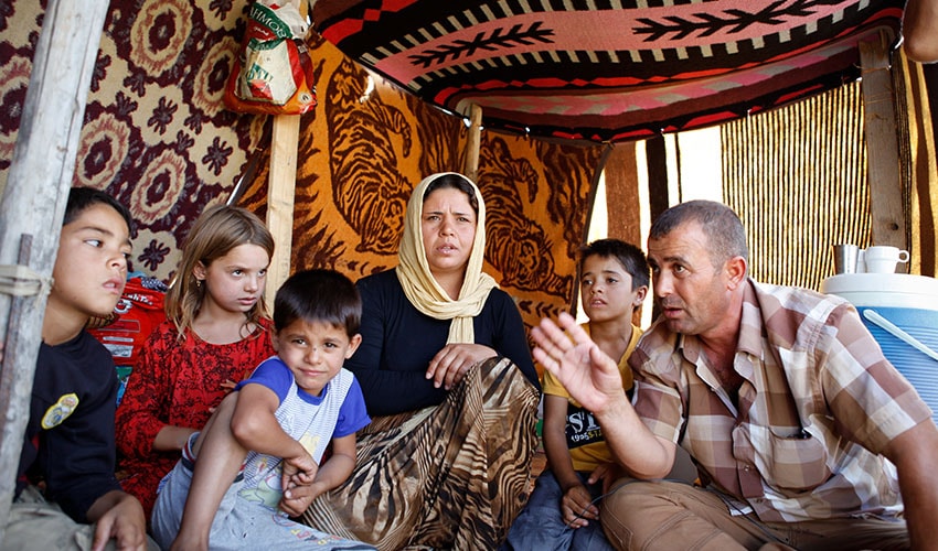 man speaking to group of five children and one woman living in makeshift camp