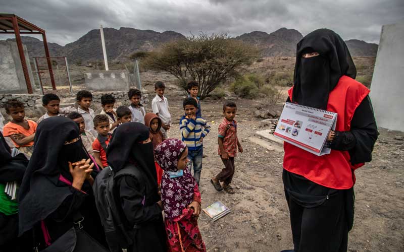A woman in Yemen, wearing a scarf which covers her face, is holding up a book to a group of children.