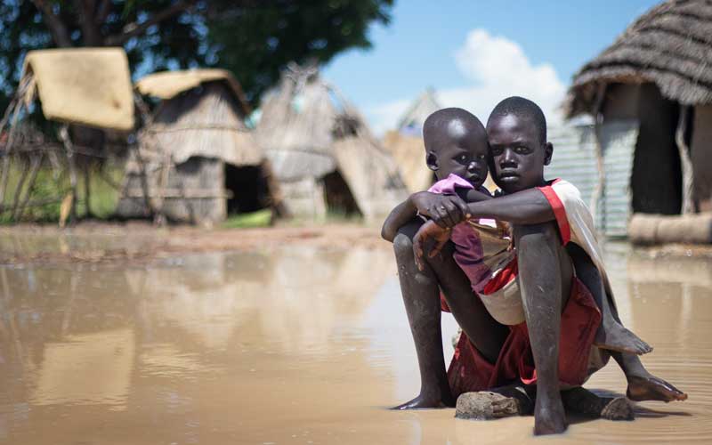 Two children perch on a rock above floodwaters in their community.