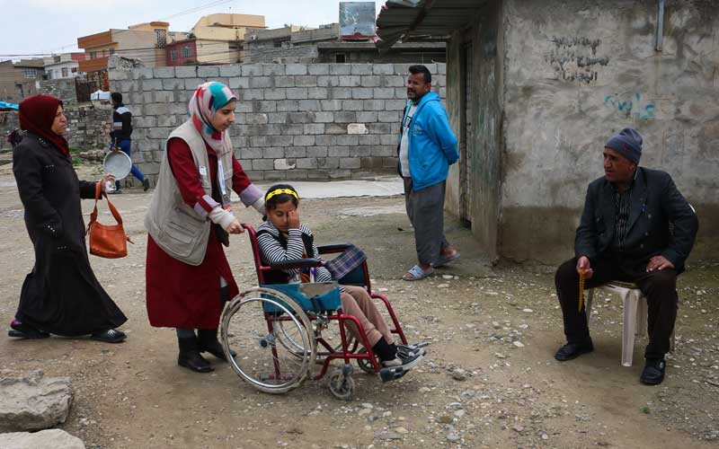 A woman wearing a head scarf pushes a girl in a wheelchair through the bombed-out streets of Mosul, Iraq.