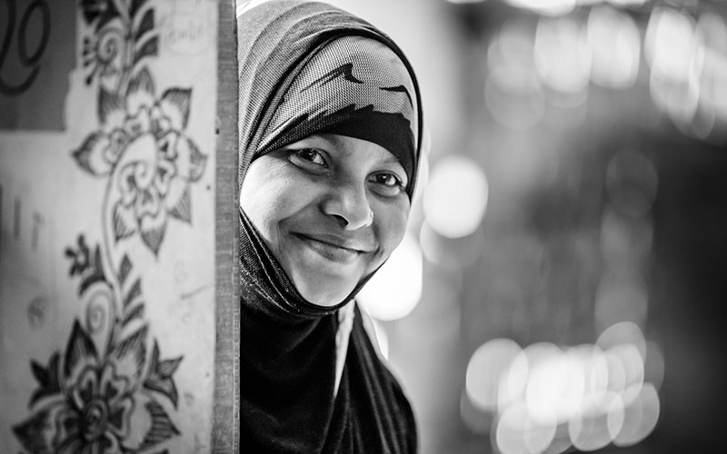 A black and white portrait of a woman with a head covering smiling.