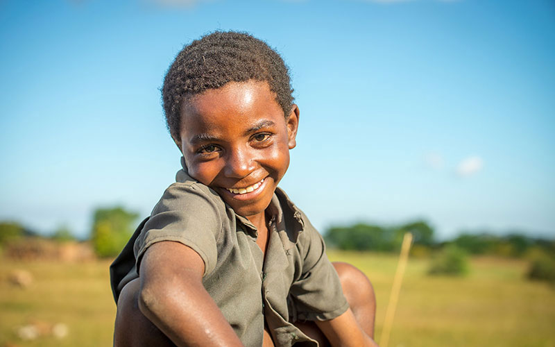 A young girl in Zambia crouches down with a big smile across her face.