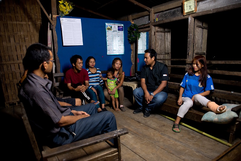 A humanitarian worker sits with a family in a wooden room.