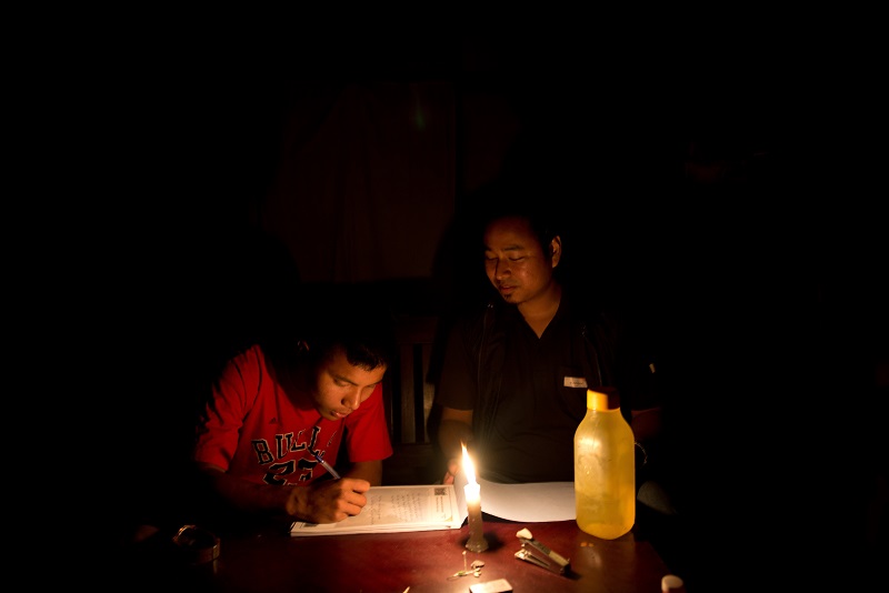 A humanitarian helps a boy write a letter by candlelight.
