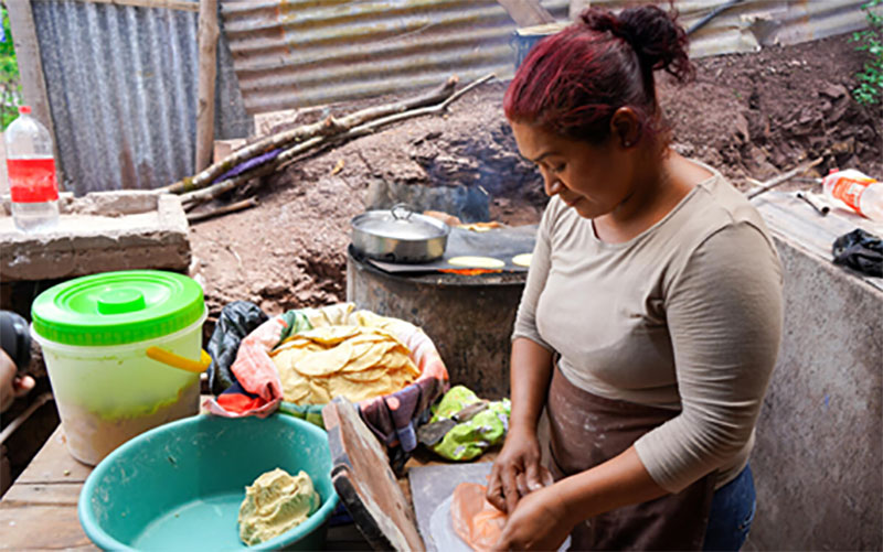 A woman unwraps food ingredients as she prepares a meal for her family.