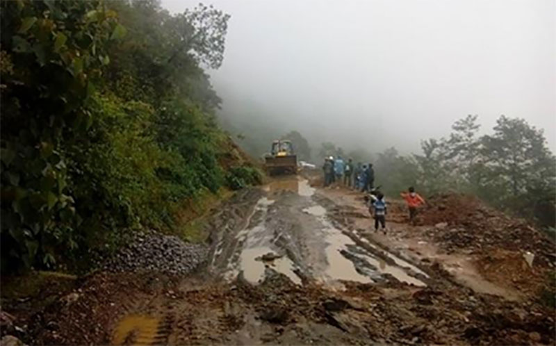 A road destroyed by a landslide and now filled with mud is being cleared by a small bulldozer.