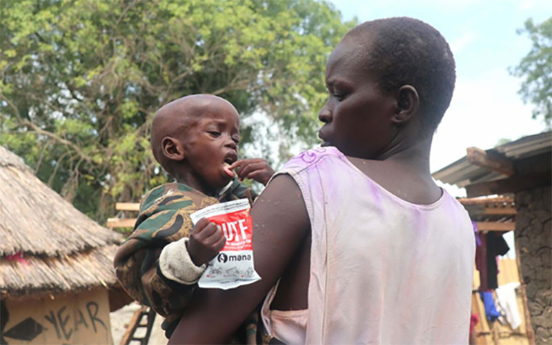 In South Sudan, a mother holds her young child. He is holding a packet of ready-to-eat high nutrient food.