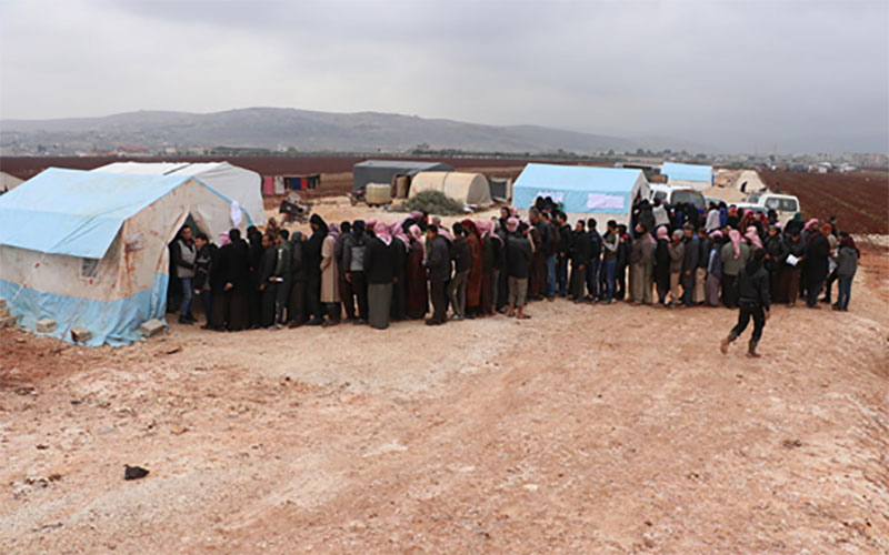 In Syria, a long line of parents waits outside a tent to receive winter clothes for their children.