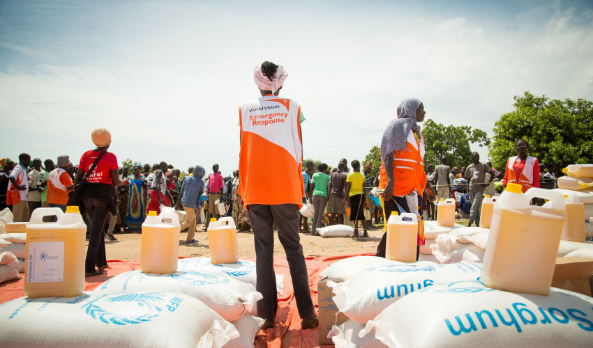A World Vision emergency response worker stands amongst bags of sorghum food aid at a refugee camp
