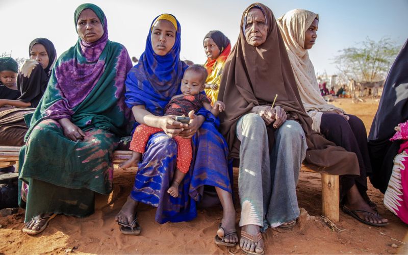 Women in Somalia sit together on a bench outside, alongside one child.