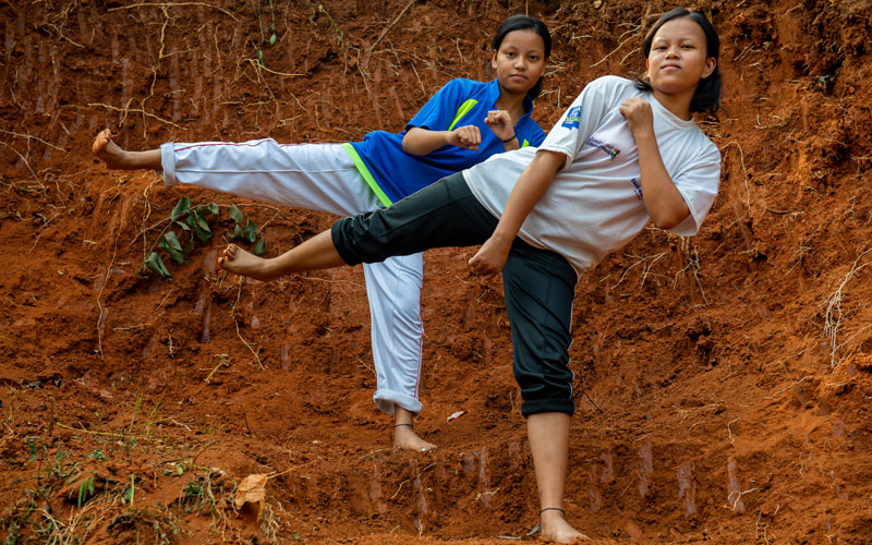 two young Indian girls stand on one leg with their other leg stretched out in a martial arts kick.