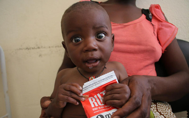 A baby holds a packet of high-nutrient, supplementary food.